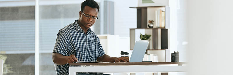 African american male entrepreneur sitting at a desk reviewing financials to determine how they will self-fund their business.