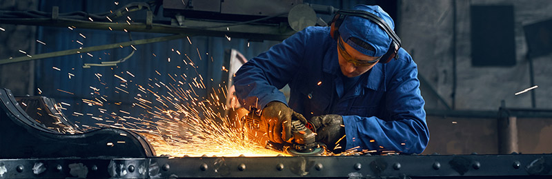 Male entrepreneur working in a machine shop on cutting through a piece of metal with sparks flying out. This is just one of the physical risks to address in his business.